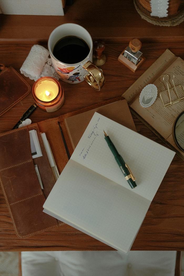 A writer's desk with an open journal, fountain pen, coffee, and a lit candle