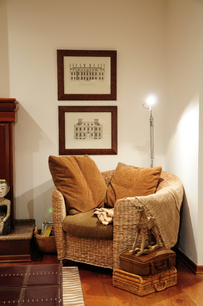 A quiet reading corner with wicker armchair, warm lamp, framed prints, and books