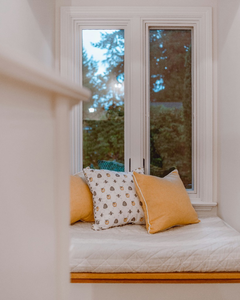 A cozy window seat reading nook with pillows looking out at trees and morning light